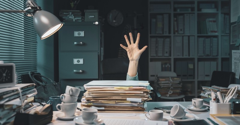 Woman sticking her hand up among paperwork and coffee