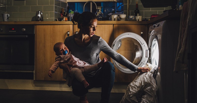 Tired stressed mom postpartum with newborn baby doing laundry chores