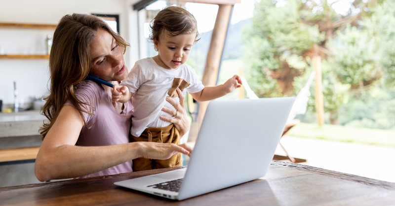 Stressed overwhelmed mom on laptop and phone with toddler kid