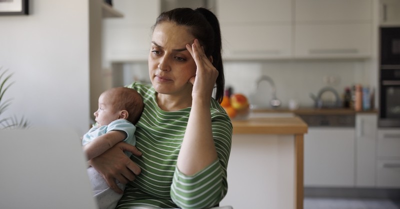 Stressed overwhelmed mom on laptop with newborn baby planning