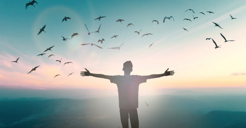 man with arms out wide at sunrise birds flying